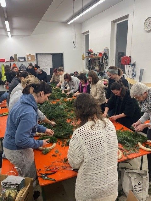 Gruppe von Frauen dekoriert einen Tisch mit grünen Kränzen. Ein weißer Beutel und eine Schachtel mit magischen Gegenständen sind in der Nähe.