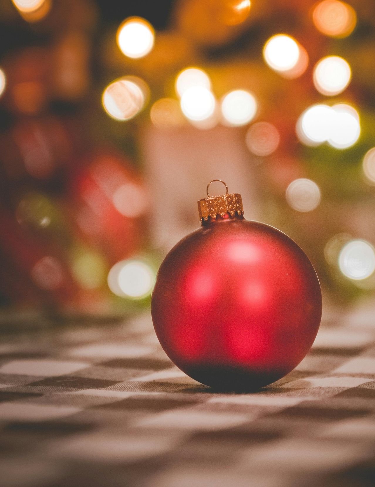 Ein Nahaufnahme einer glänzenden roten Weihnachtskugel auf einer strukturierten Oberfläche mit verschwommenen festlichen Lichtern im Hintergrund.
