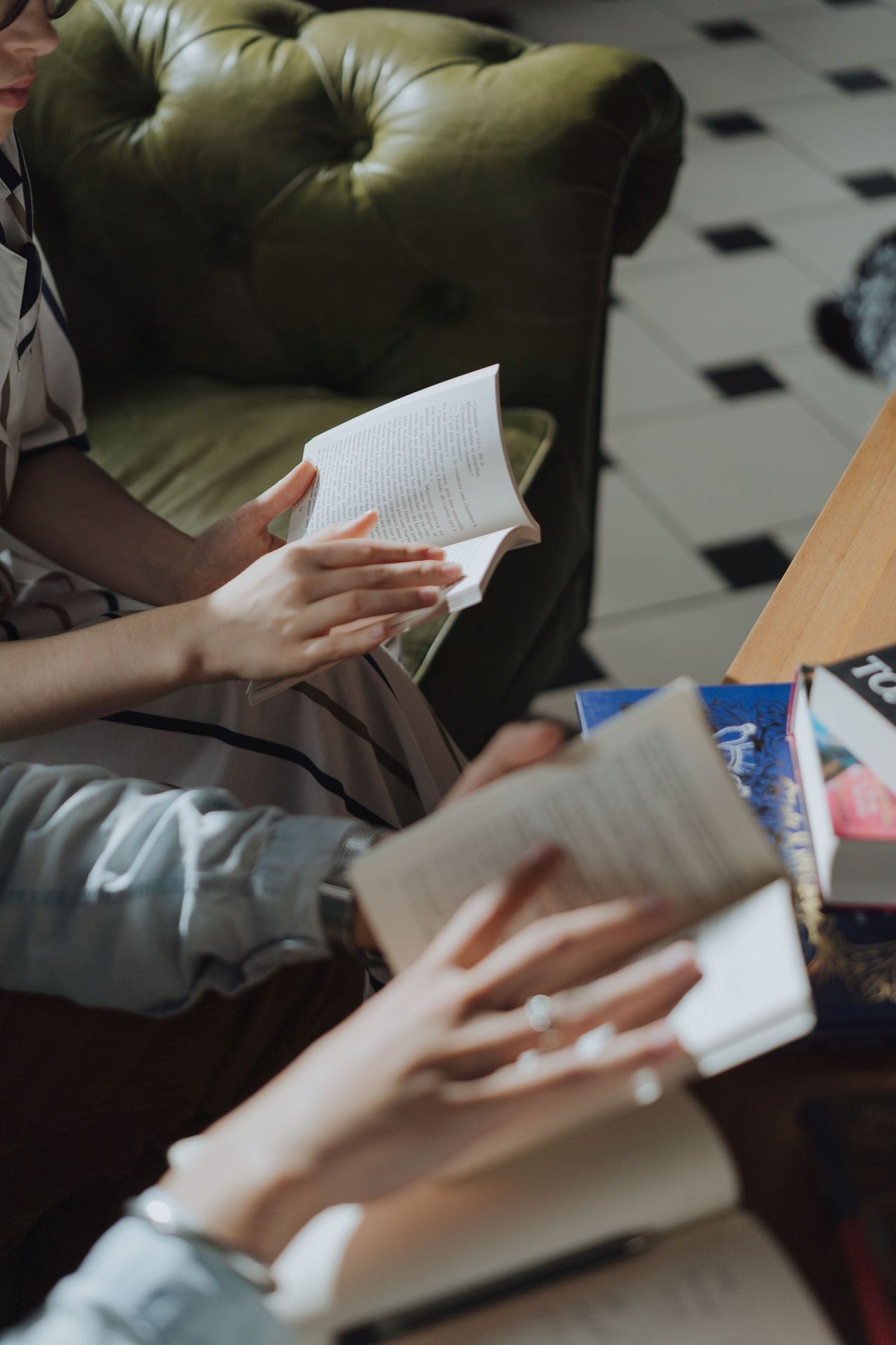 Two people are sitting on a couch, reading books. One person is wearing a ring and the other is wearing a bracelet.