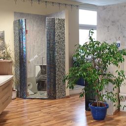 Ein modernes Badezimmer mit Holzboden verfügt über eine Glasdusche und eine große Pflanze. Ein Fenster an der Wand sorgt für natürliches Licht.