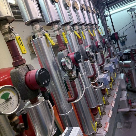 Ein Nahaufnahme einer Reihe von metallischen Rohren und Messgeräten in einer industriellen Umgebung, mit gelben Etiketten und roten Schläuchen sichtbar.