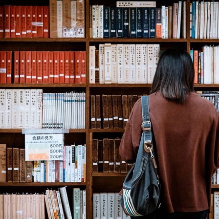 Bild enthält, Book, Library, Adult, Female, Person, Woman, Furniture, Shelf, Bookcase, Handbag