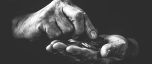 Zwei ältere Hände halten Münzen in einem Schwarz-Weiß-Foto, was finanzielle Stabilität oder Wohltätigkeit symbolisiert.