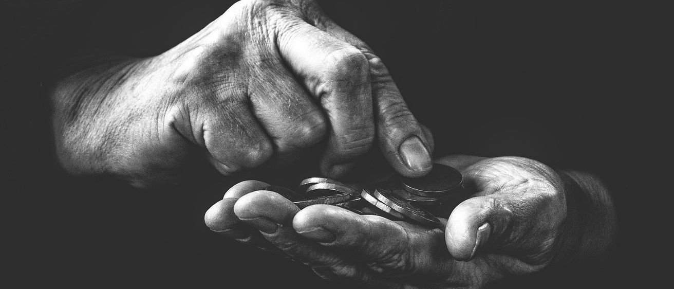 Zwei ältere Hände halten Münzen in einem Schwarz-Weiß-Foto, was finanzielle Stabilität oder Wohltätigkeit symbolisiert.