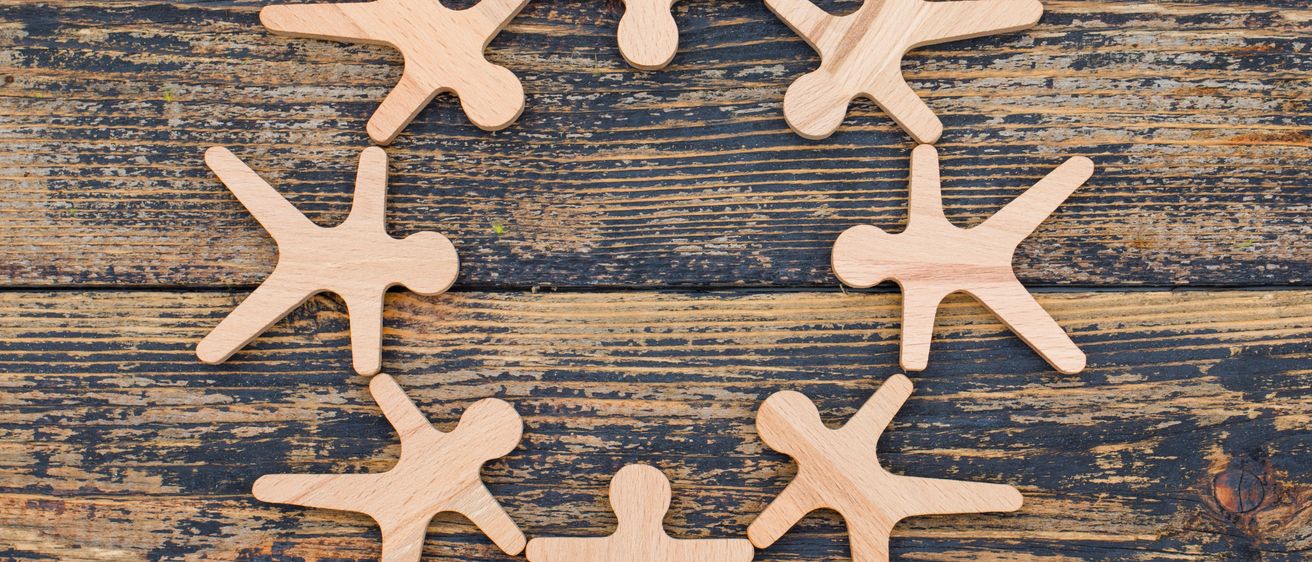 Eine kreisförmige Anordnung von Holz-Stickfiguren auf einer Holzoberfläche. Die Figuren sind in einem kreisförmigen Muster angeordnet.