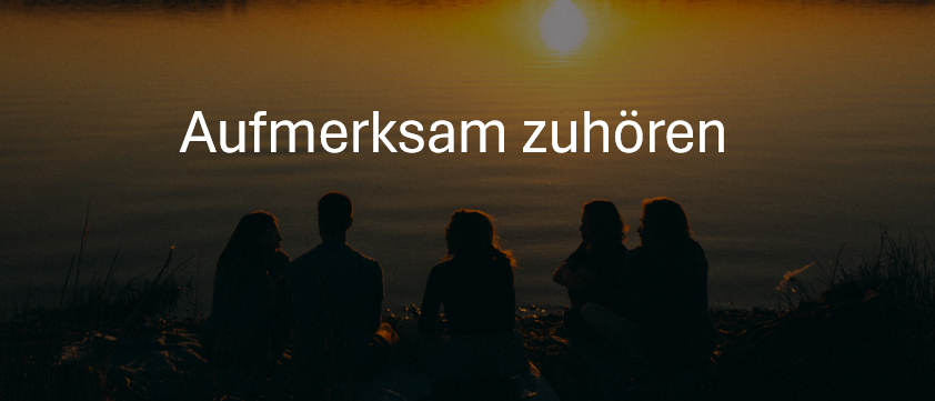Fünf Menschen sitzen am Ufer eines Sees, während die Sonne im Hintergrund untergeht. Der Text lautet 'Aufmerksam zuhören'.
