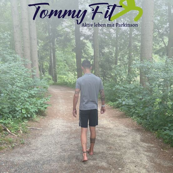 Ein Mann geht barfuß auf einem Waldpfad, trägt ein graues T-Shirt und schwarze Shorts. Der Pfad ist von hohen Bäumen und Grün umgeben. Die Worte 'Tommy Fit' und 'Aktiv leben mit Parkinson' erscheinen oben.