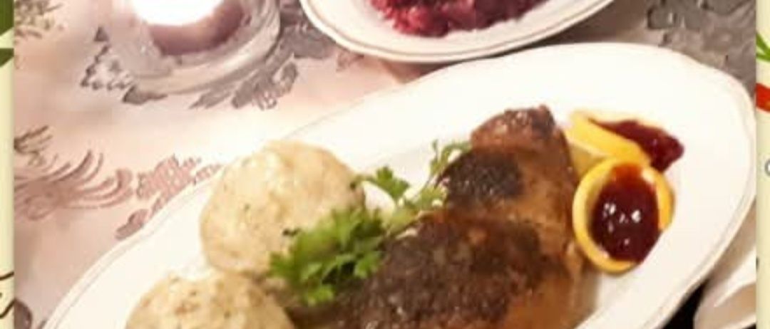 Zwei weiße Teller mit Essen. Ein Teller hat gebratenes Fleisch, Kartoffelpüree und eine Beilage mit roter Sauce. Der andere Teller hat Rote-Bete-Salat und Butter. Eine Kerze auf einem Tisch.