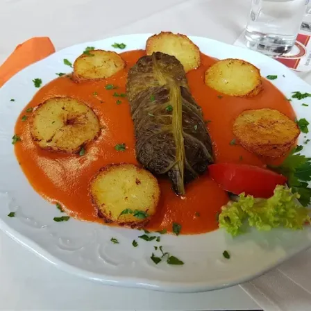 Ein weißer Teller mit Tomatensauce, frittierten Kartoffelscheiben und einem eingerollten Kohlblatt mit Petersilie und einer Tomate.