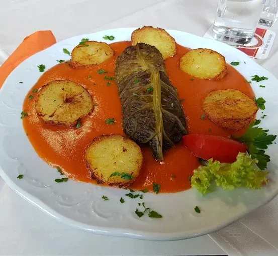 Ein weißer Teller mit Tomatensauce, frittierten Kartoffelscheiben und einem eingerollten Kohlblatt mit Petersilie und einer Tomate.