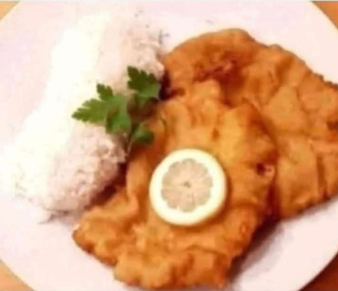 A plate of fried bread with a lemon slice and parsley on top, accompanied by a serving of rice.