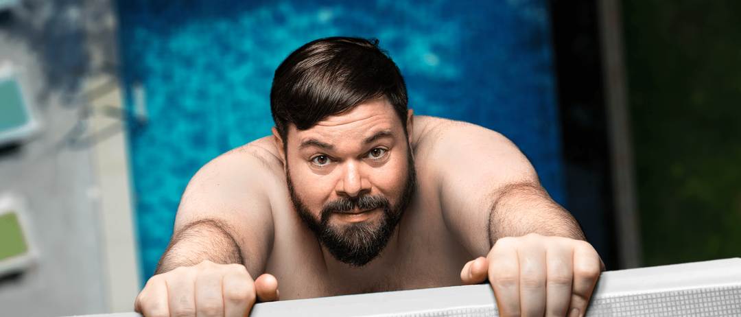 Ein Mann mit Bart lehnt über den Rand eines Pools und sieht überrascht in die Kamera. Seine Arme ruhen auf dem Rand. Der Pool ist sauber und blau.