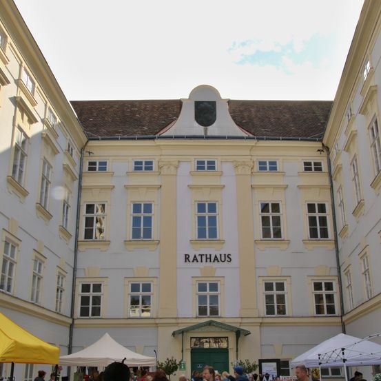 Ein traditionelles europäisches Gebäude mit dem Wort Rathaus über dem Eingang. Es hat viele Fenster und ist von Zelten umgeben.
