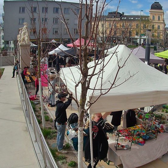 Ein Außenmarkt mit mehreren Zelten, Menschen beim Stöbern und Einkaufen, und einem klaren blauen Himmel im Hintergrund.
