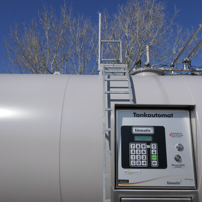 Ein weißer Tank hat eine Metallleiter und ein elektronisches Bedienfeld. Das Bedienfeld ist mit 'Tankautomat limatic' beschriftet. Das Bedienfeld hat eine Tastatur mit Zahlen und Symbolen, einen Bildschirm und Tasten.