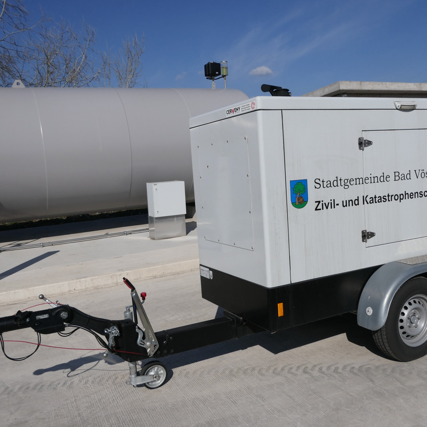 Ein weißer Anhänger mit einem Logo für Zivil- und Katastrophenschutz ist neben einem großen Lagertank geparkt.