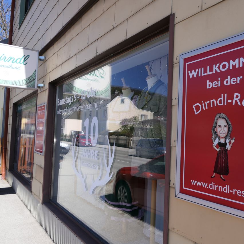 Ein Schaufenster zeigt ein rotes Schild mit einer Comicfigur, die Kunden willkommen heißt. Das Fenster zeigt ein Grafik-Jubiläum von 10 Jahren und die Reflexion eines roten Autos.