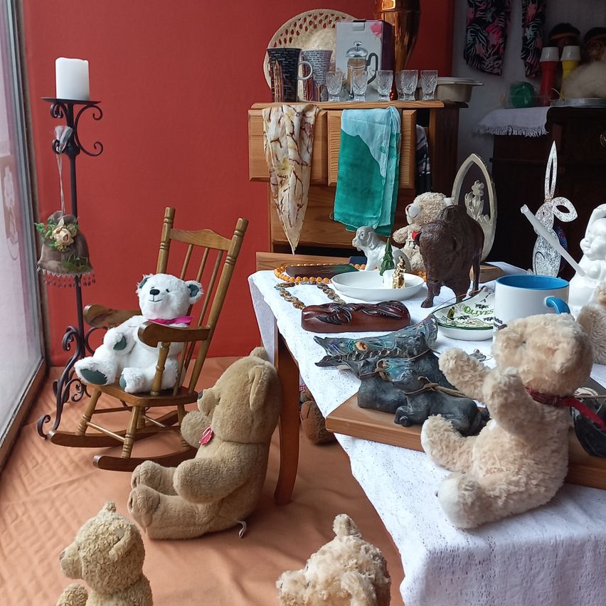 Ein Raum mit einer roten Wand, einem hölzernen Schaukelstuhl und einem Tisch mit verschiedenen Gegenständen, einschließlich Plüschtieren, einer Kerze und einer weißen Tischdecke.
