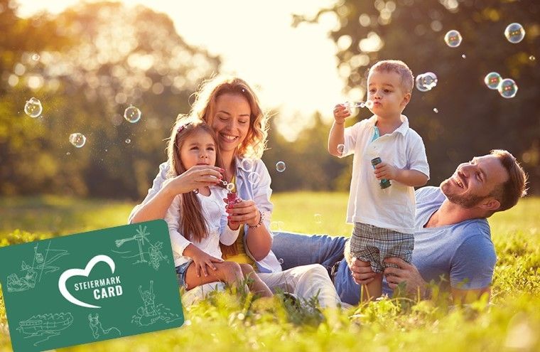 Eine Familie im Park, zwei Kinder spielen mit Seifenblasen und Eltern lächeln. Eine grüne Karte mit 'Steiermark Card' ist sichtbar.