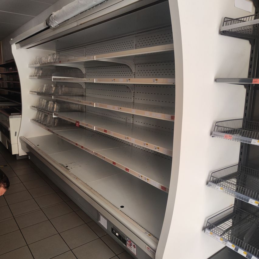 Ein leerer Kühlvitrine mit Metallregalen in einem Laden. Im Vordergrund ist der Kopf einer Person zu sehen.
