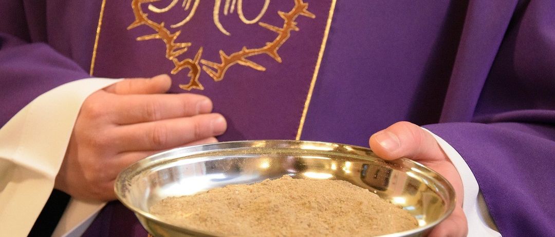 Eine Person in einem violetten Gewand hält eine Schale mit braunem Pulver. Das Gewand hat goldene Muster.