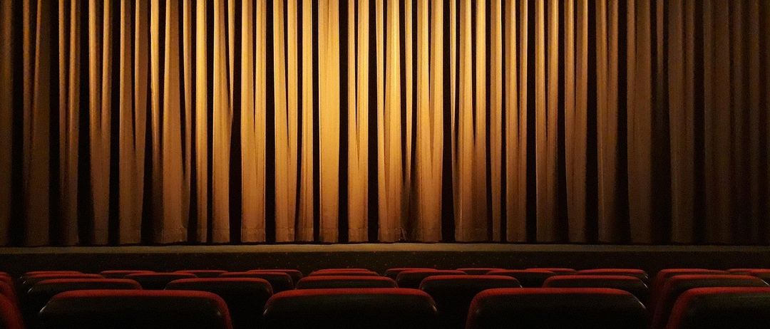 Ein leeres Kino mit Reihen roter Sitze unter geschlossenen Vorhängen und gedämpftem Licht.