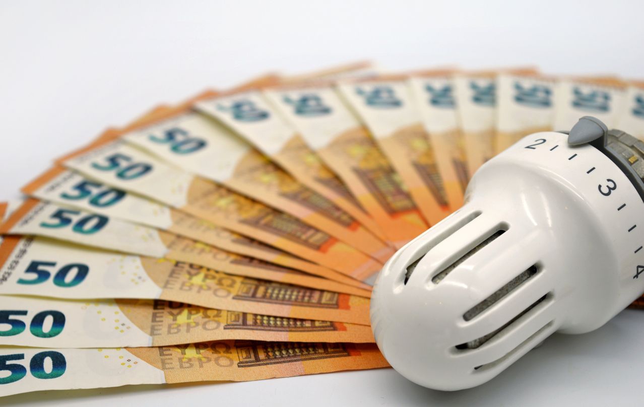 Euro bills are fanned out on a white surface, with a white thermostat in the foreground.