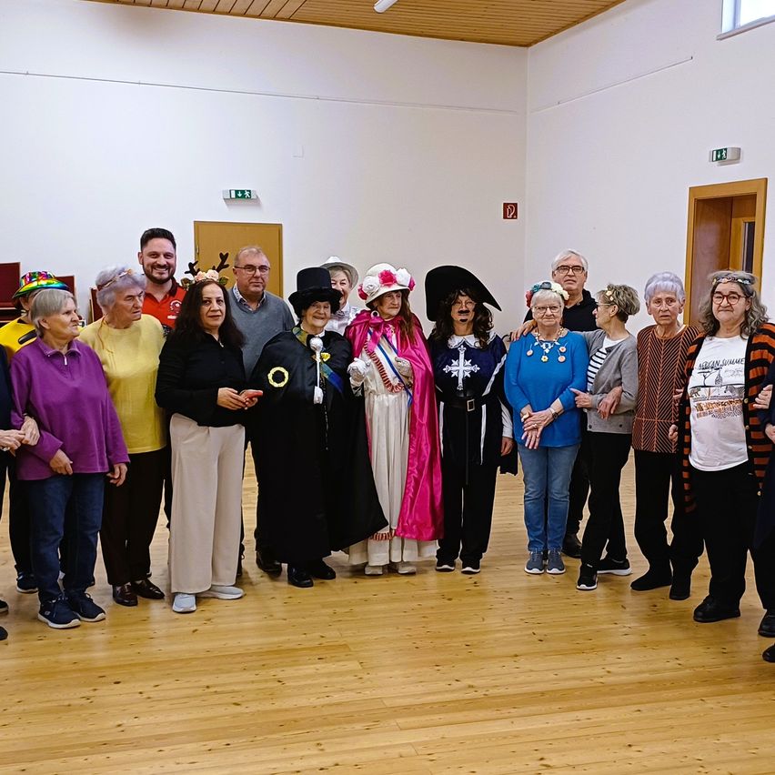 A group of people in a room, some in costumes, smiling for a photo. One woman in a pirate hat.