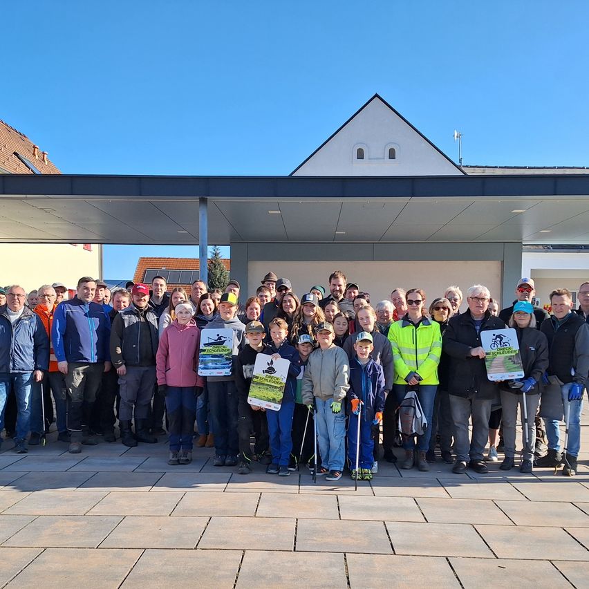 Eine Gruppe von Menschen, einige in Jacken und Handschuhen, posiert für ein Foto vor einem Gebäude mit blauem Dach. Einige halten Plakate.