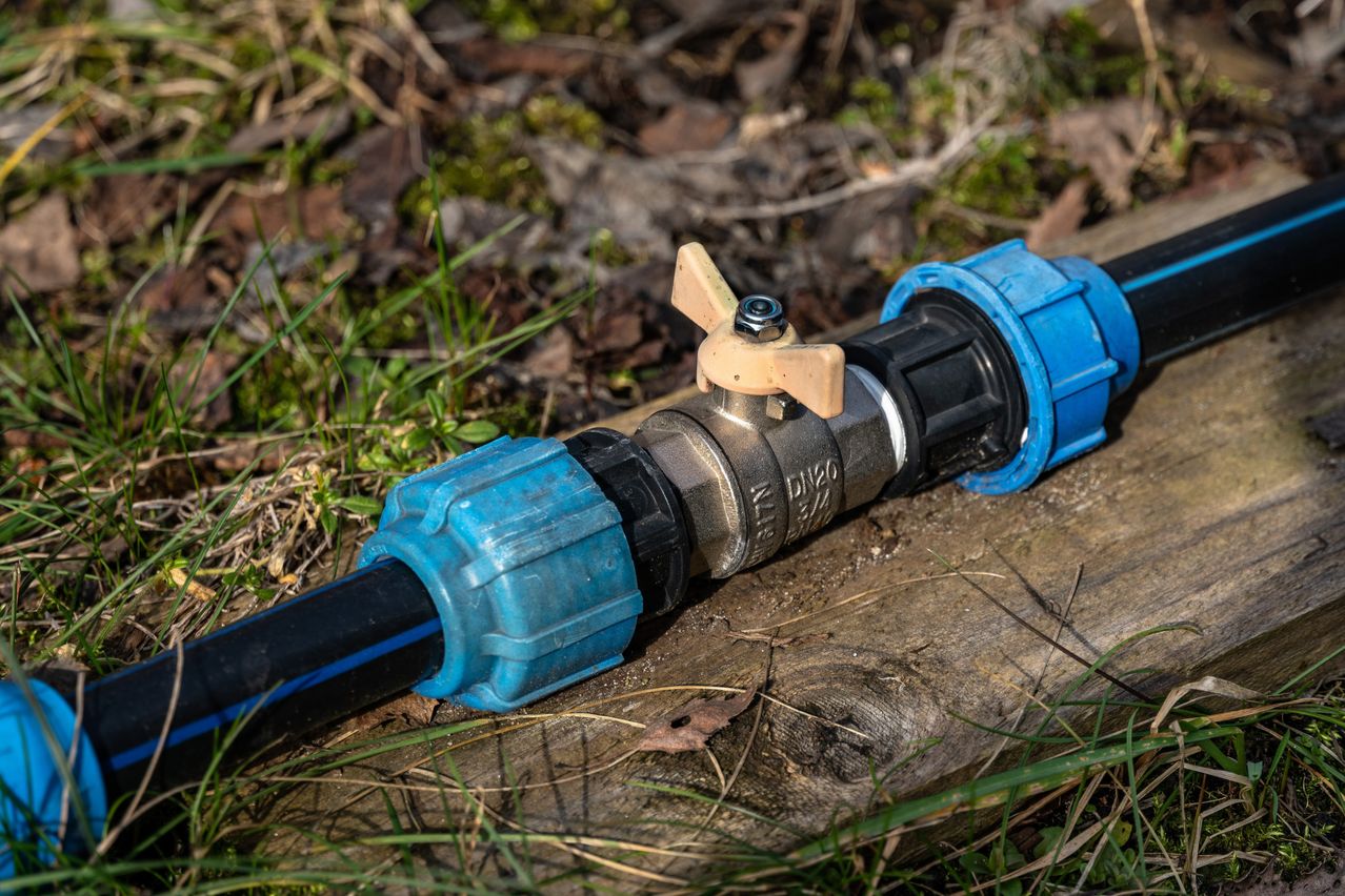 Wasserhahn mit blauen Kunststoffverschraubungen auf einem schwarzen Rohr im Freien