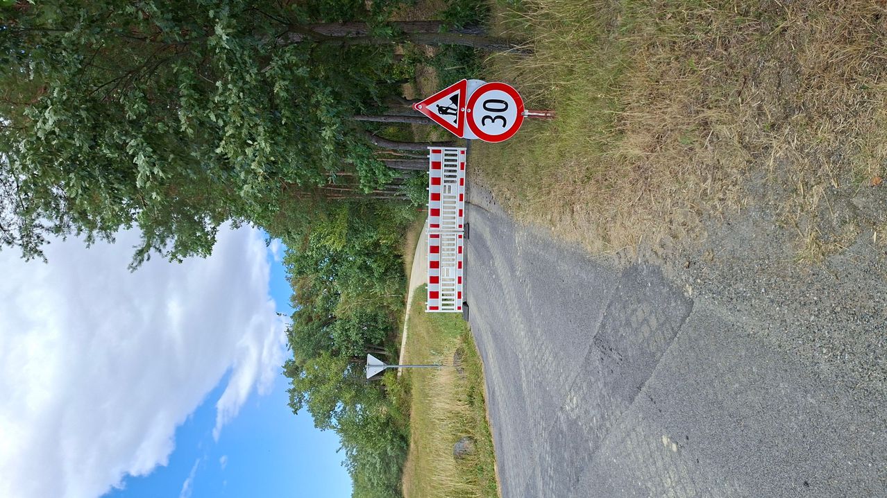 Eine Straße mit einem Geschwindigkeitslimit von 30 und einem dreieckigen Warnzeichen in der Nähe eines Tores an einem sonnigen Tag.
