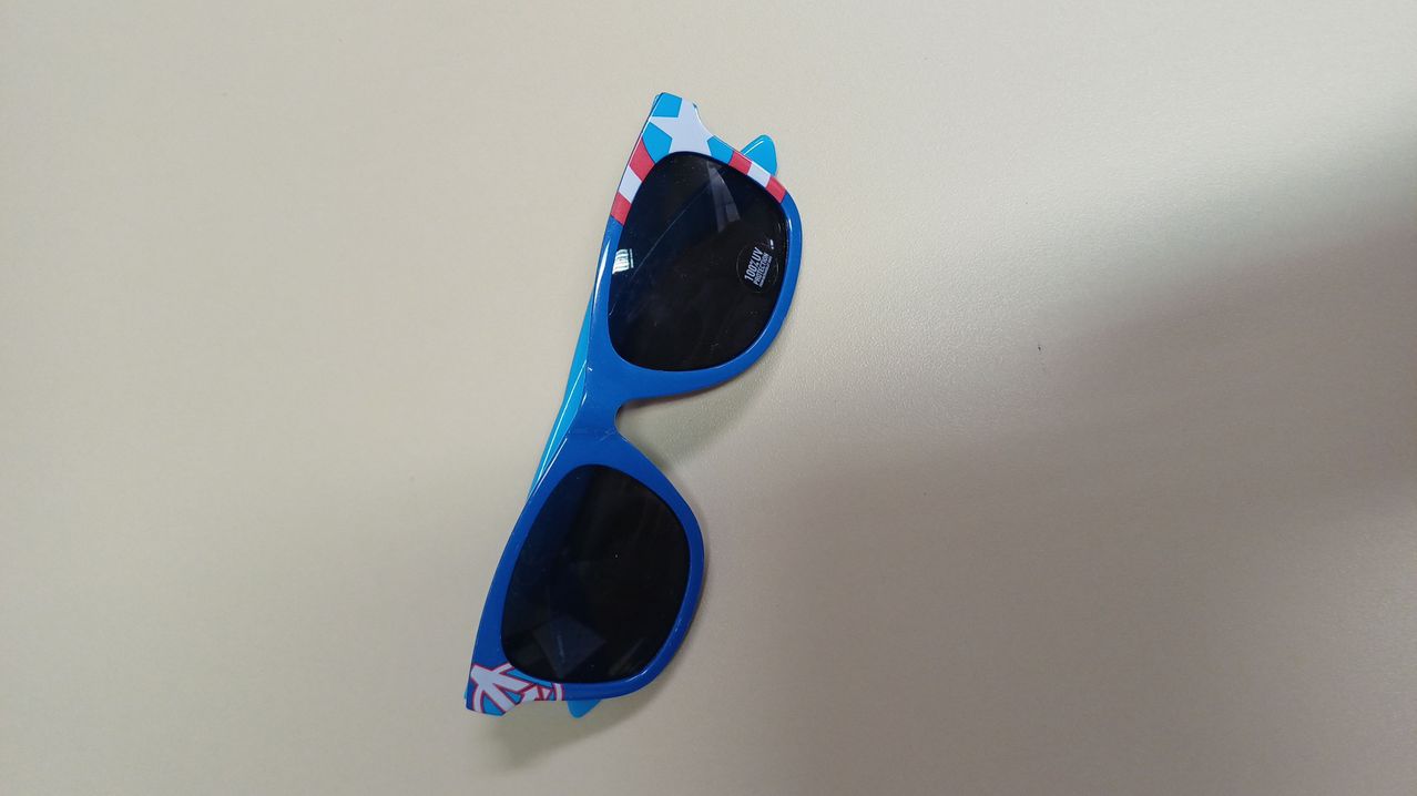 Ein Paar blauer Sonnenbrille mit einem amerikanischen Flaggendesign an den Armen, schwarzen Gläsern und weißem Text an den Bügeln.