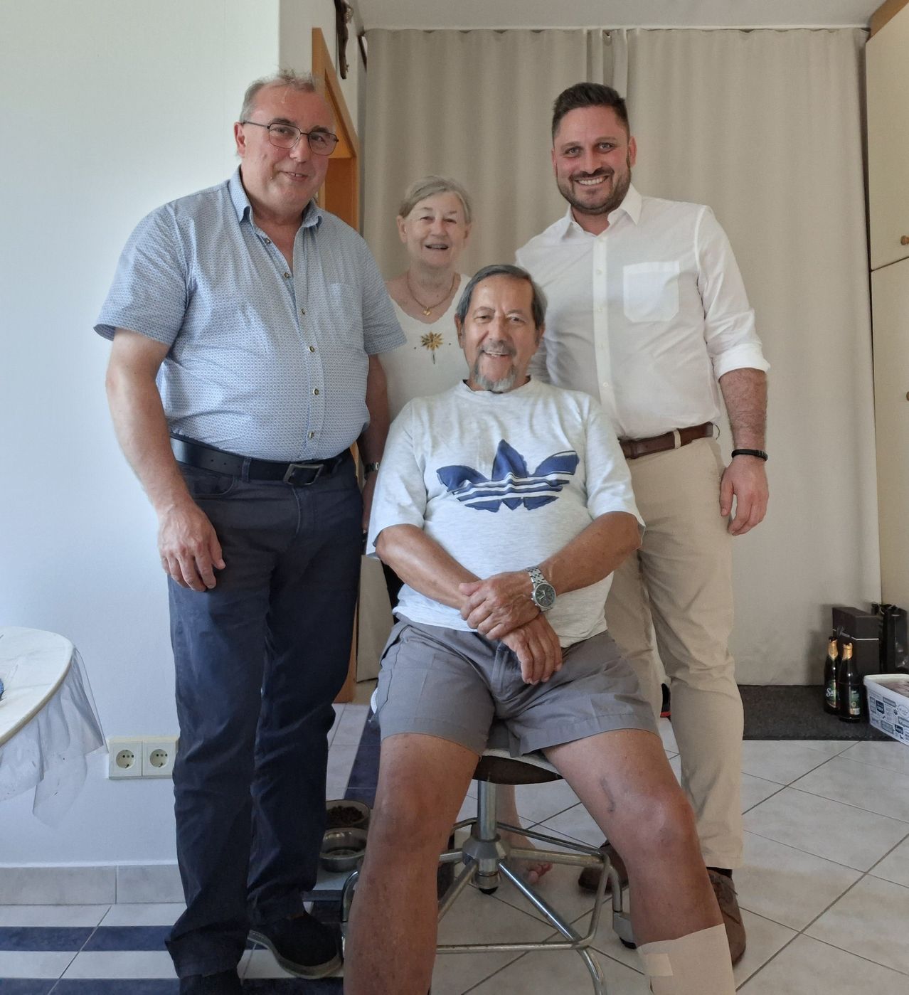 Four people pose for a photo. The man in the center sits on a stool. Behind him, a woman stands. Two men stand beside them.