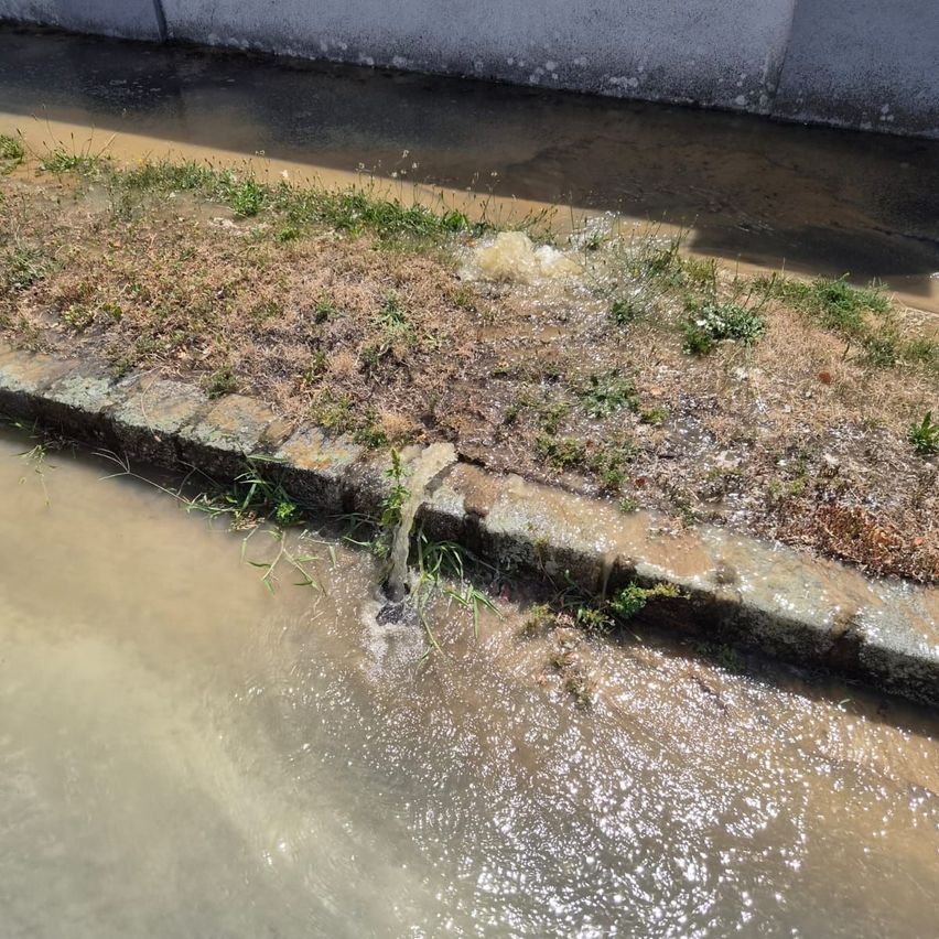 Eine Wasserleitung leckt in einen Entwässerungskanal und lässt Wasser auf den Bürgersteig sickern.
