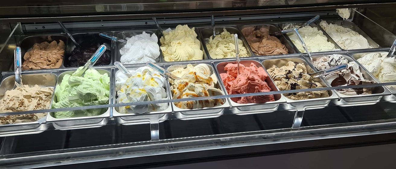 Eine Vitrine mit verschiedenen Eissorten, darunter weiß, gelb, rosa und grün.