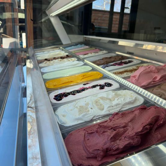 Eine Vitrine mit verschiedenen Eissorten. Das Eis kommt in mehreren Farben, einschließlich weiß, gelb, rosa und braun.