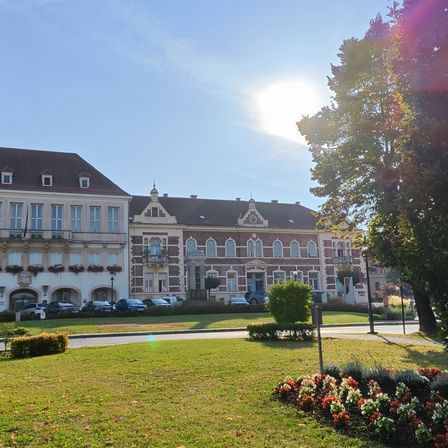Ein großes Gebäude mit vielen Fenstern und einem braunen Dach ist von einem gepflegten Rasen und mehreren geparkten Autos umgeben.