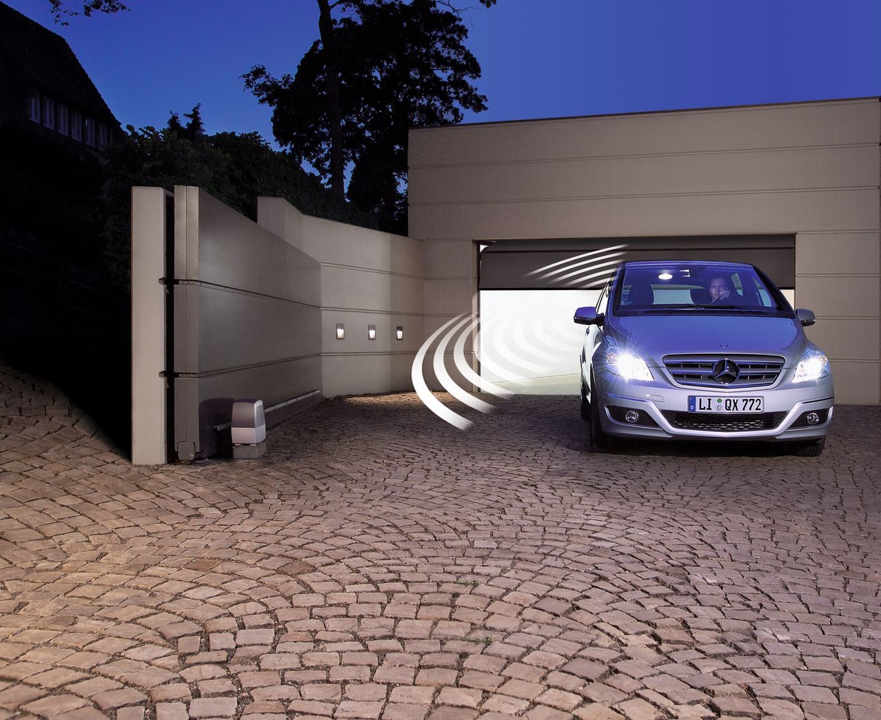 Ein Mercedes-Benz Auto fährt bei Nacht in eine Garage mit geschlossenem Tor und beleuchtetem Weg.