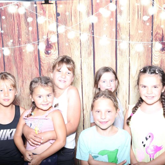 Eine Gruppe von fünf jungen Mädchen posiert für ein Foto vor einer Holzwand mit Lichterketten.