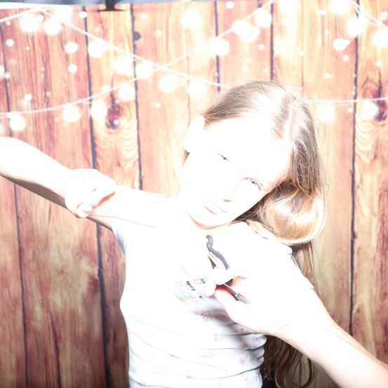 Ein junges Mädchen mit blonden Haaren posiert für ein Foto mit einer Schere in der Hand vor einem hölzernen Hintergrund.