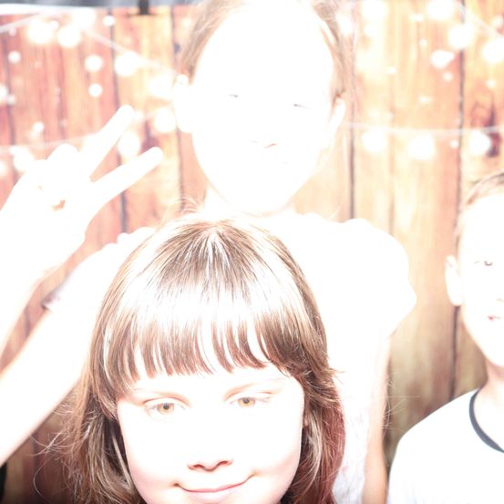 Ein verschwommenes Foto zeigt drei Kinder, wobei ein Mädchen im Vordergrund eine Friedensgeste macht. Der Hintergrund ist eine Holzwand.