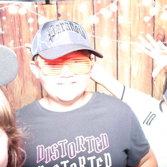 Ein junger Mann in einer Batman-Kappe und neongelben Gläsern lächelt. Hinter ihm steht eine weitere Person, die ein weißes Shirt mit der Nummer 10 trägt.