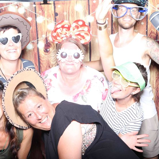 Eine Gruppe von Menschen mit Hüten und Sonnenbrillen lächelt und posiert für ein Foto vor einer Holzwand.