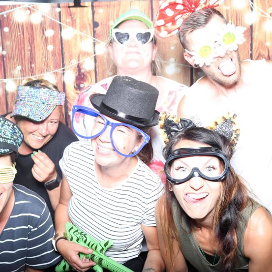 Eine Gruppe von Menschen, die Sonnenbrillen, Hüte und Stirnbänder tragen, posiert für ein Foto. Einer streckt die Zunge heraus. Sie alle scheinen Spaß zu haben.