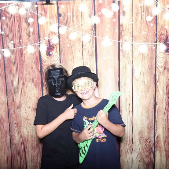 Zwei Jungen stehen vor einer Holzwand mit Lichterketten. Ein Junge trägt eine Darth-Vader-Maske und der andere hält eine grüne Gitarre.