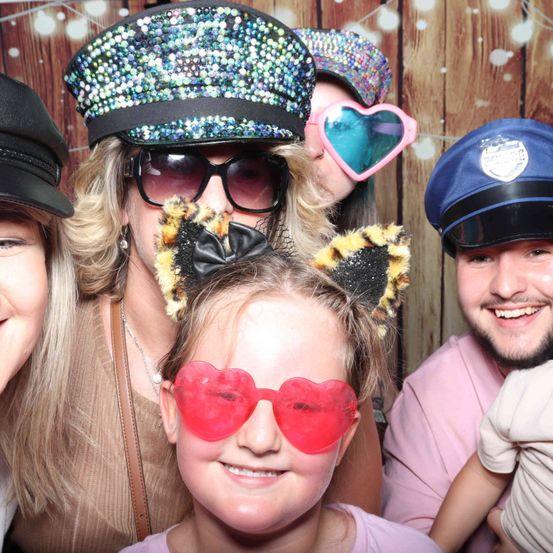 Eine Gruppe von Menschen posiert für ein Foto, trägt verschiedene Hüte und Brillen, mit einem hölzernen Hintergrund.