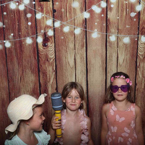 Drei junge Mädchen posieren für ein Foto in einem Fotokabine. Sie haben Lichterketten im Hintergrund und eine hält ein Mikrofon.