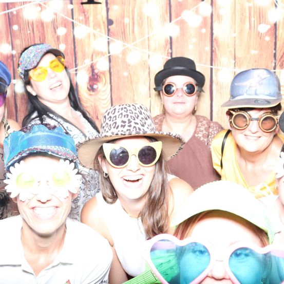 Eine Gruppe von Menschen in verschiedenen Hüten und Sonnenbrillen lächelt und posiert für ein Foto vor einem hölzernen Hintergrund.