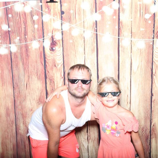 Ein Mann und ein junges Mädchen mit Pixelbrillen posieren für ein Foto vor einem hölzernen Hintergrund.