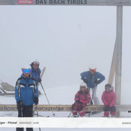 Eine Gruppe von Menschen skifahren auf einem verschneiten Hang. Sie tragen Helme, Schutzbrillen und Skianzüge. Das Holzschild zeigt PITZTAL DAS DACH TIROLS. Das Foto hat einen Wasserzeichen mit dem Text HOCHER PITTAL 04/03/2023 14:46.